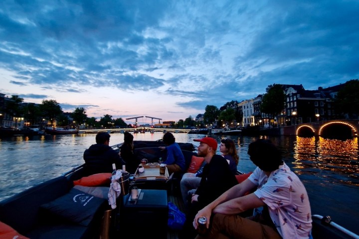 a group of people sitting in an open boat in front of Magerebrug Amsterdam