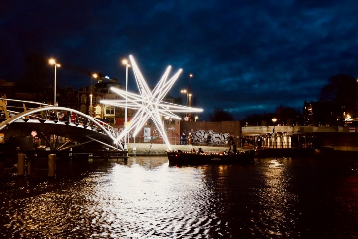 A bridge spanning a body of water, accompanied by a large star-shaped light art installation, with a small open boat cruising nearby